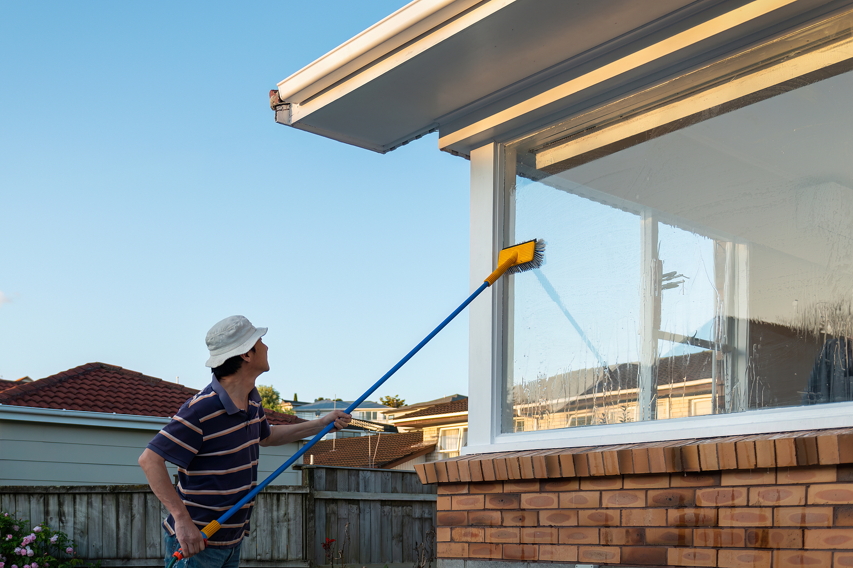 Man washing windows with long pole and brush. Home maintenance projec.