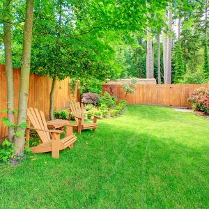 Fenced backyard with green lawn, flower beds and romantic sitting area with wooden chairs and table