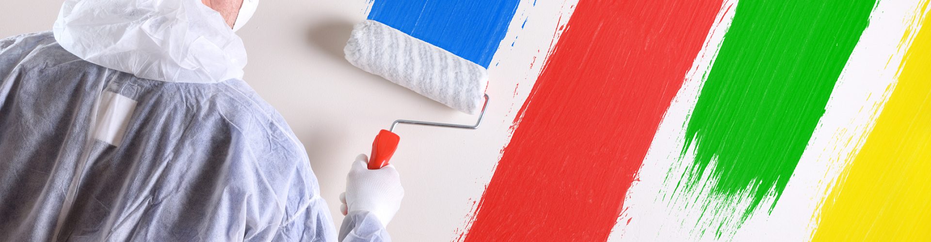 Background with professional painter with working overalls and roller on the back of a white wall painted with four colors. Horizontal composition.